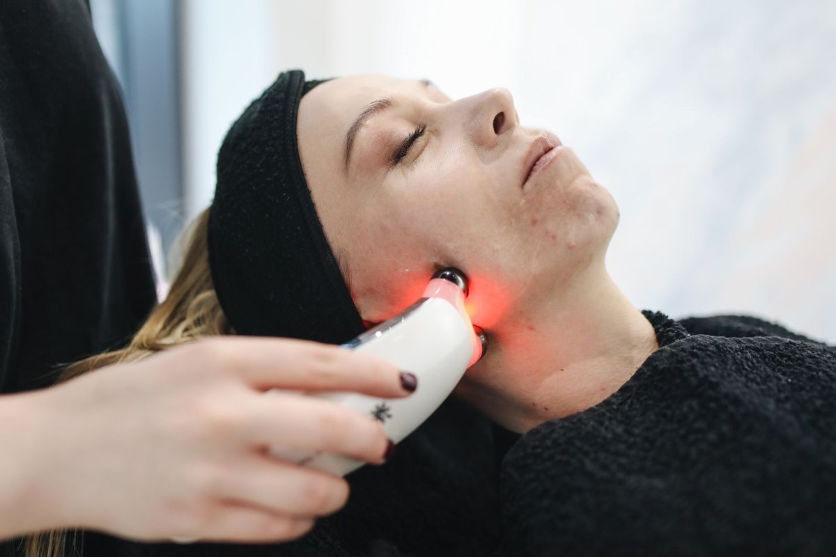Practitioner holding a handheld red-light device against a client's jawline