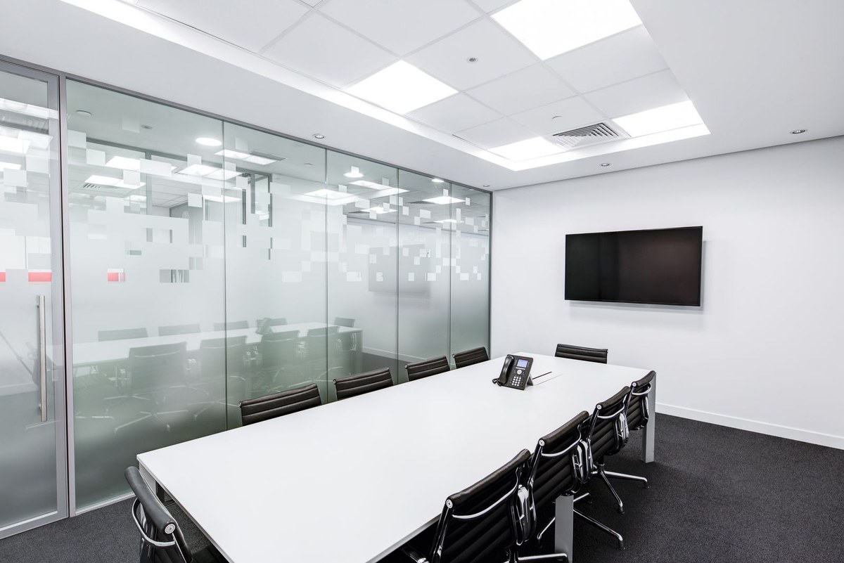 Empty modern conference room with a white table, black chairs, wall TV, and frosted glass partition