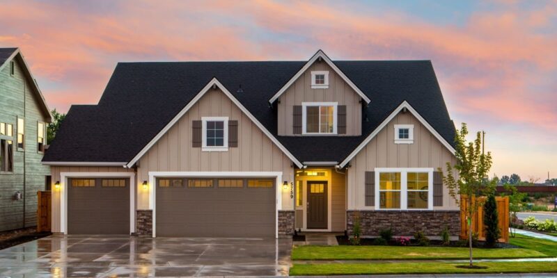 Craftsman-style two-storey house with three-car garage and stone accents lit at sunset above a wet driveway