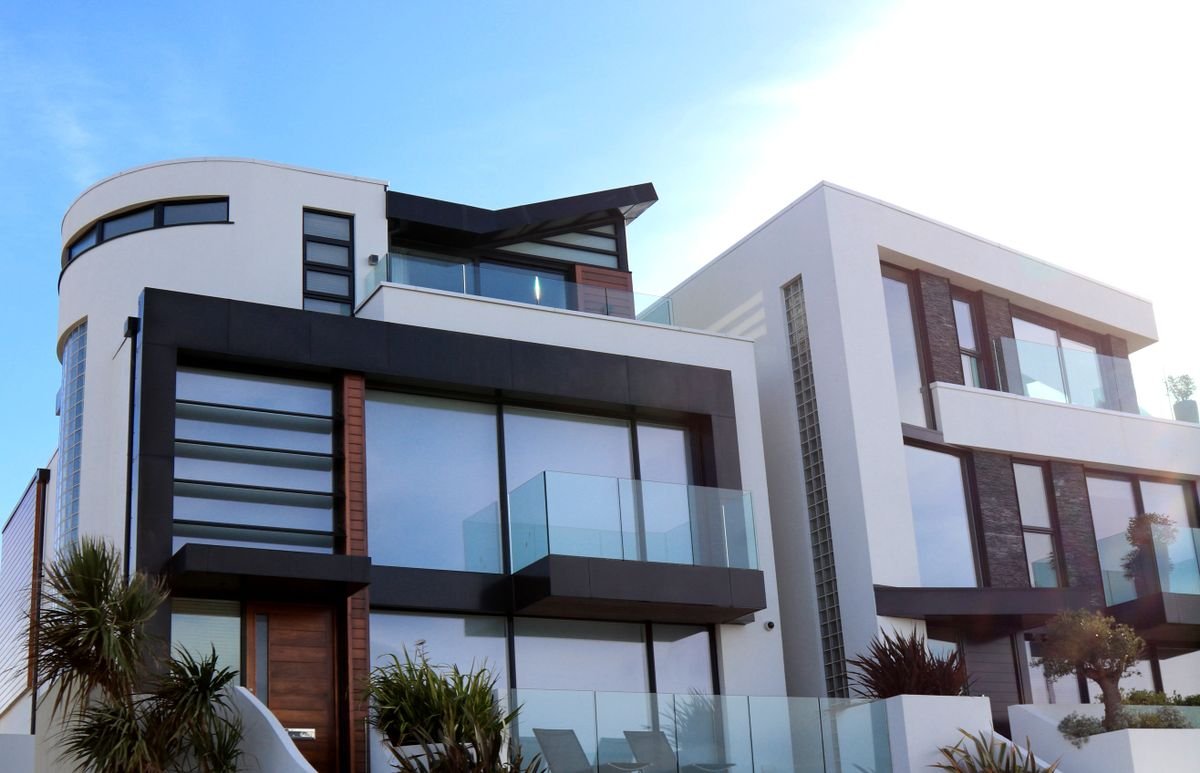 Low-angle view of a modern white and dark grey multi-storey house with glass balconies under a clear blue sky